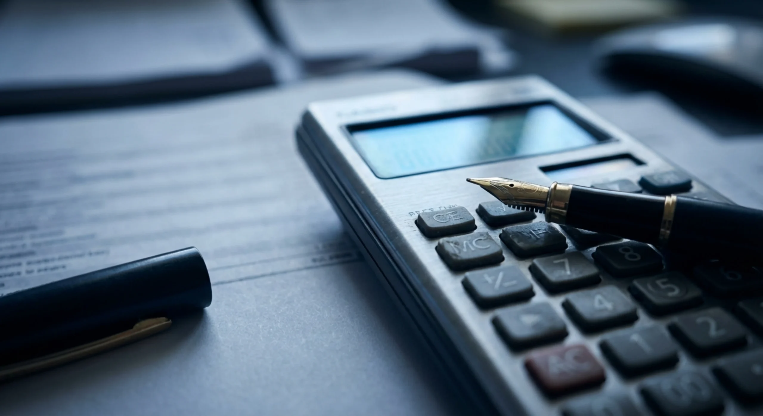 Gros plan macro sur une calculatrice et un stylo posés sur un tableau de tarifs.