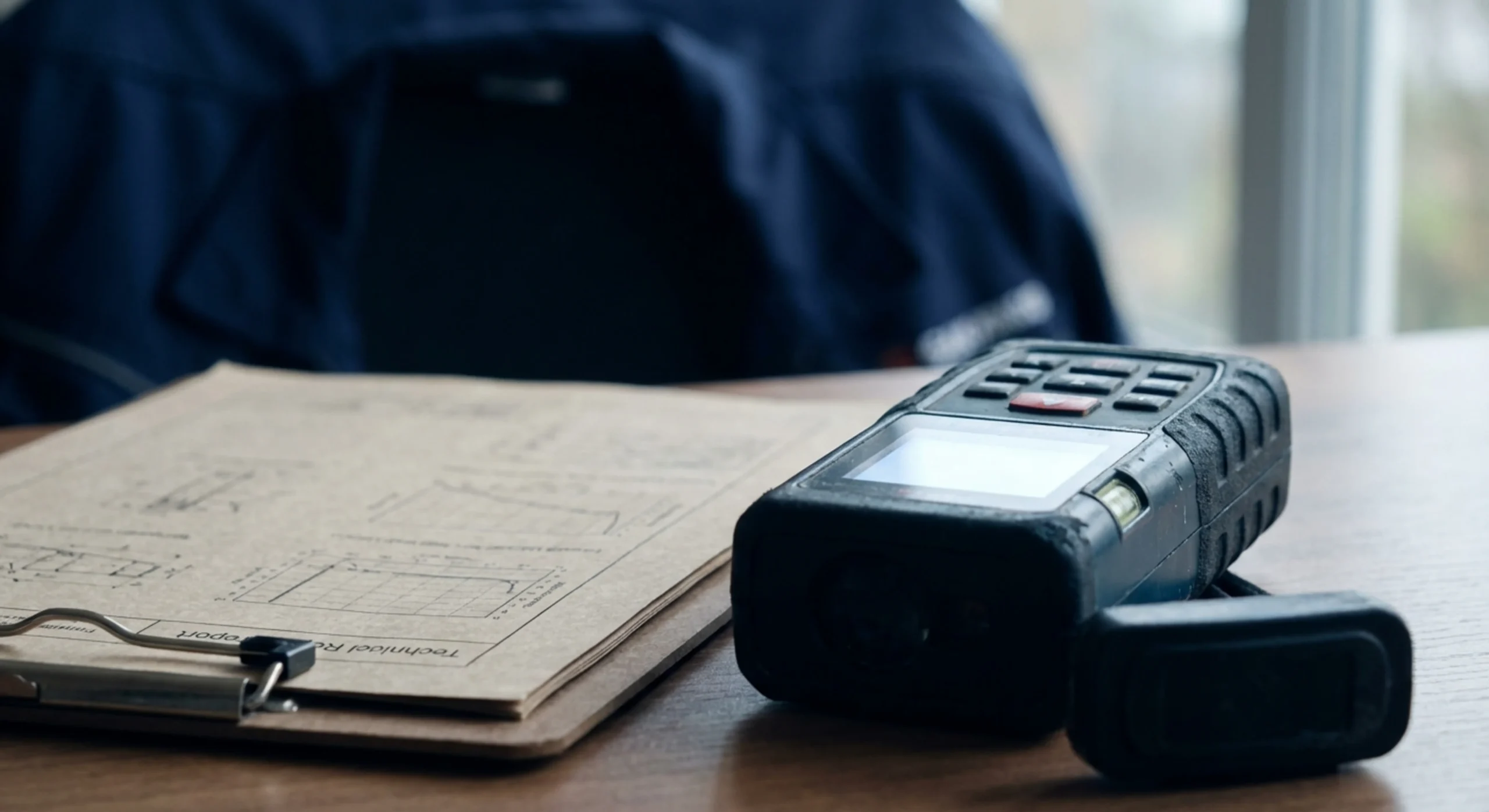 Gros plan sur un télémètre laser et des documents de diagnostic immobilier technique.